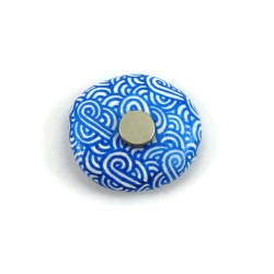 Magnet réalisé avec un faux galet rond peint blanc aux volutes bleues métallisées