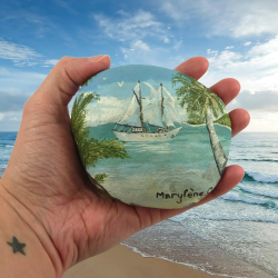 Galet peint représentant un voilier vu d'une île tropicale