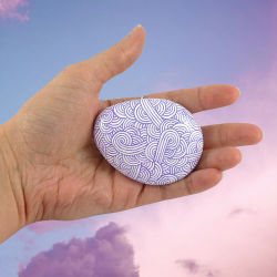 Painted pebble with purple doodles on white background