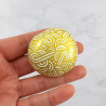 Small painted pebble with golden doodles on white background